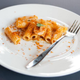 Half-eaten plate of pasta with tomato sauce with a fork